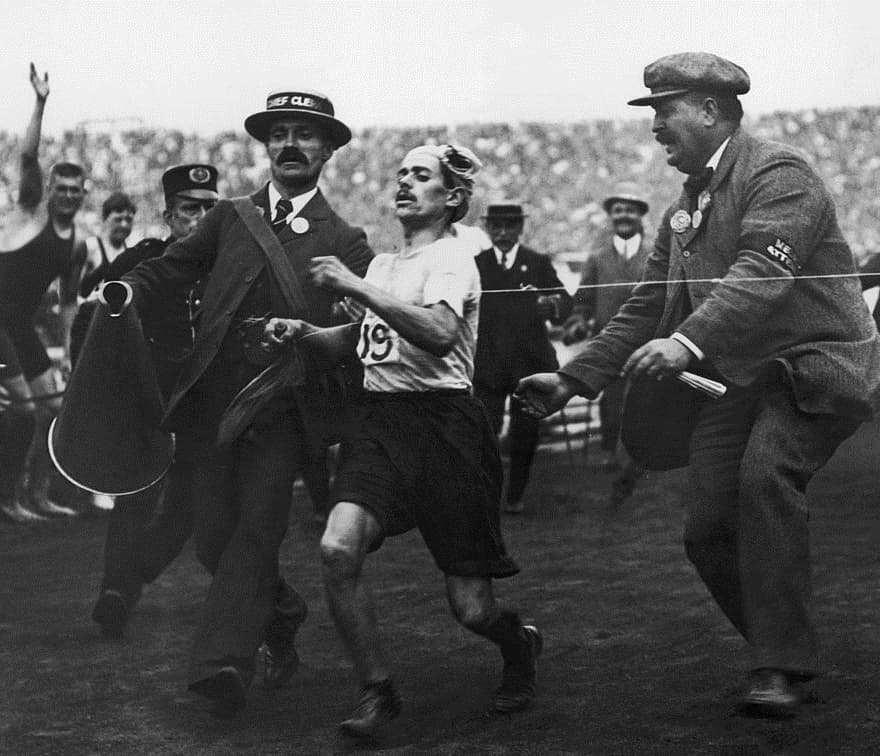 Dorando Pietri, exhausted, being helped across the finish line of the 1908 Olympic marathon.