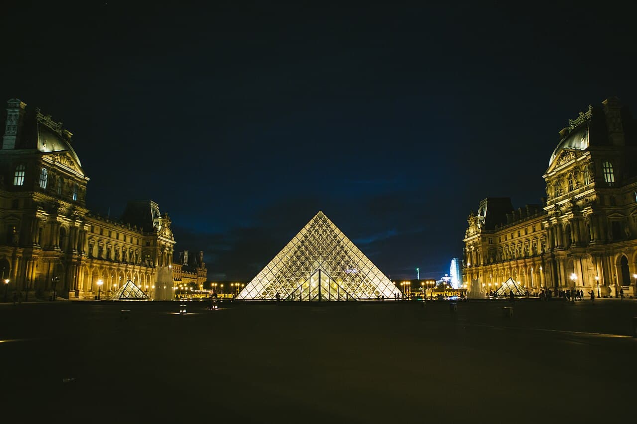 The glass and metal Louvre Pyramid illuminated at night in the Cour Napoléon courtyard in Paris.