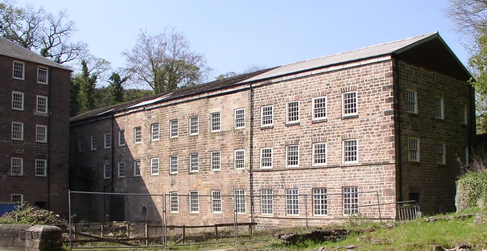 The original 1771 mill building at Cromford, a tall multi-storey stone factory in Derbyshire's Derwent Valley.