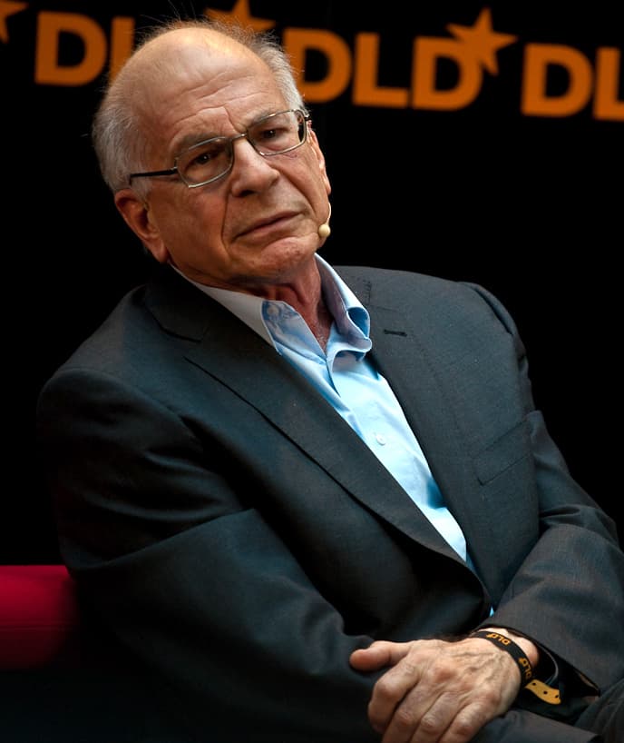 Psychologist Daniel Kahneman, an older man with glasses and a dark jacket, seated on stage at a conference.