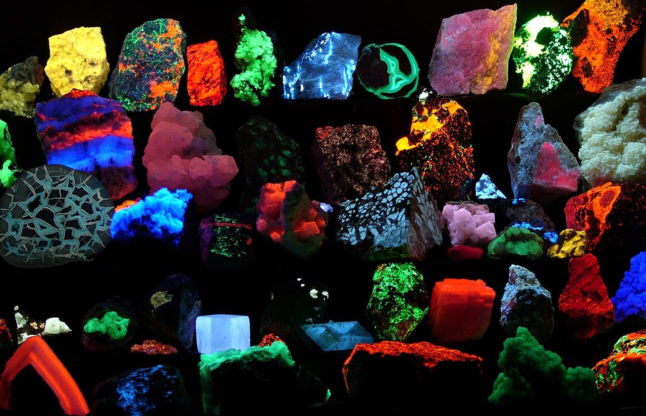 A collection of rocks glowing in vivid green, orange, red and blue under ultraviolet lamps in the dark.