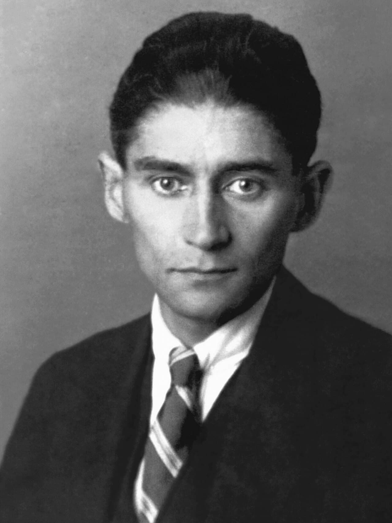 Black-and-white portrait photograph of a thin young man with dark hair and large dark eyes, wearing a suit and tie.