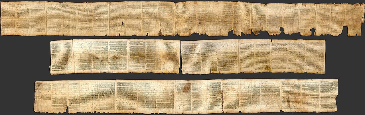 A long strip of aged, light-brown parchment covered in neat columns of Hebrew script, with a few darker patches and tears.