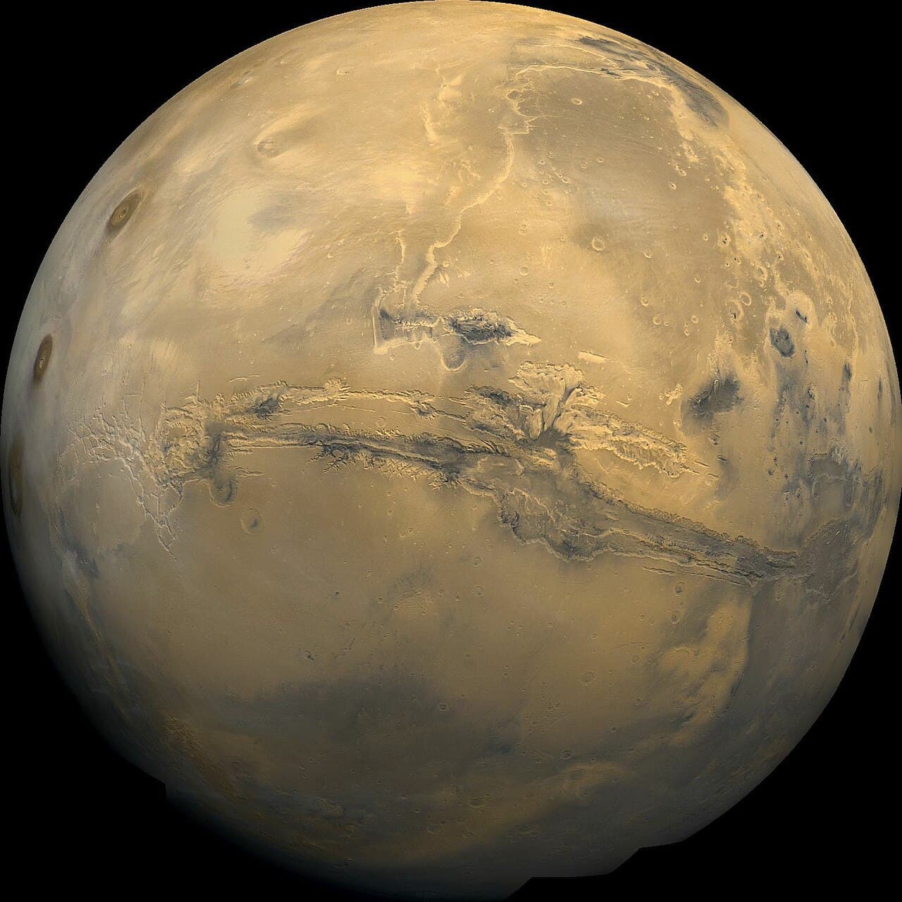 Mars seen from space, a rusty orange globe with darker grey patches and the long canyon system Valles Marineris across its middle.