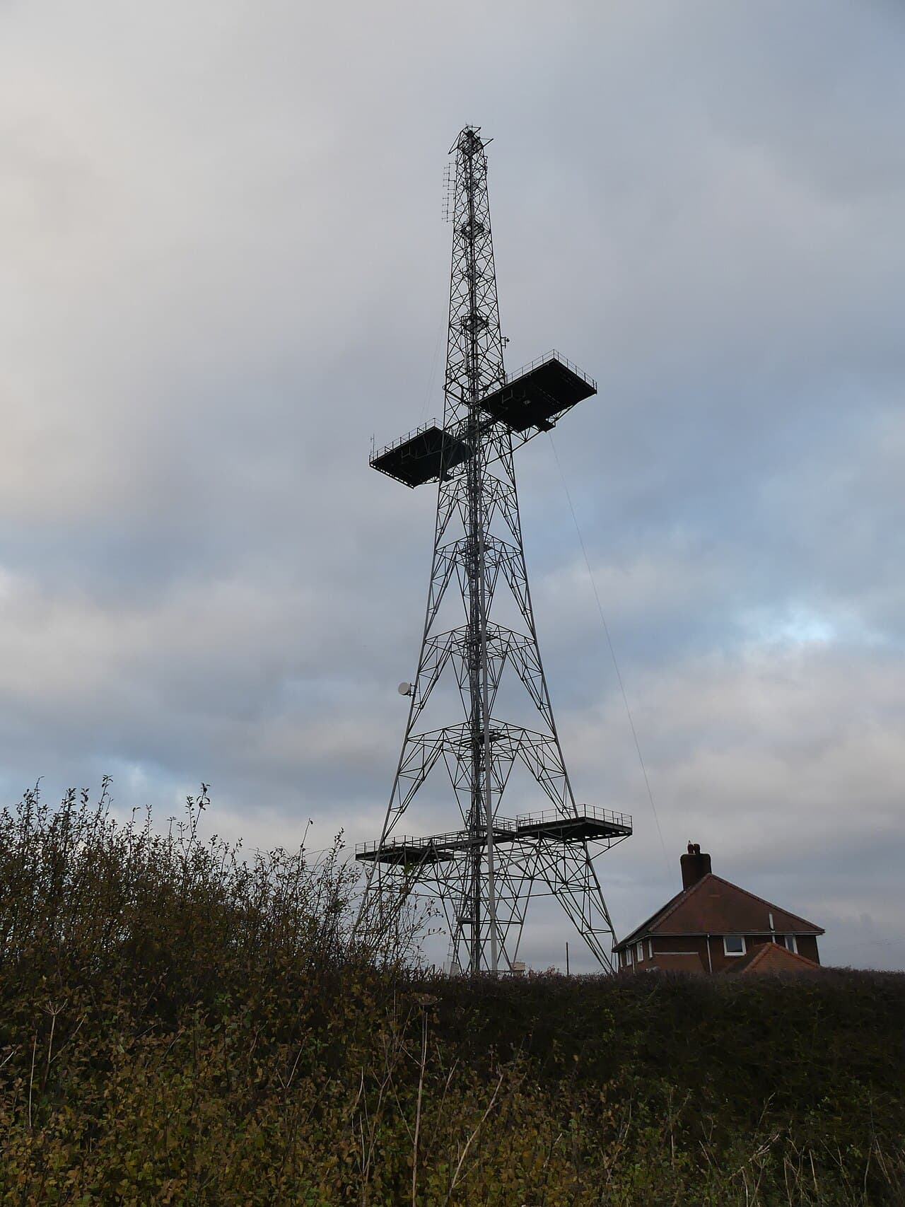 A tall steel lattice radio tower standing in a green field, a surviving transmitter mast from the Chain Home radar network.