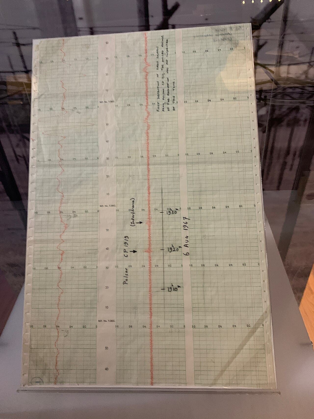A strip of chart-recorder paper with a wavy pen trace and handwritten notes, showing the signal of the first pulsar.