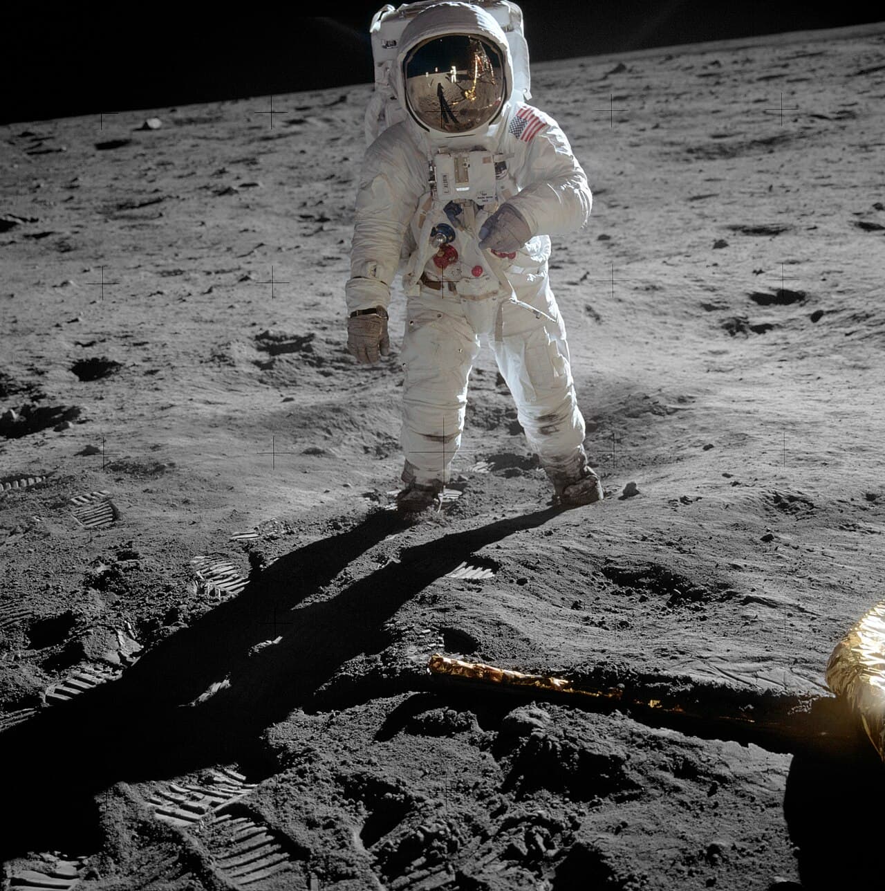 Buzz Aldrin standing on the Moon's surface in a white spacesuit, photographed by Neil Armstrong, with the lunar module Eagle reflected in his visor.