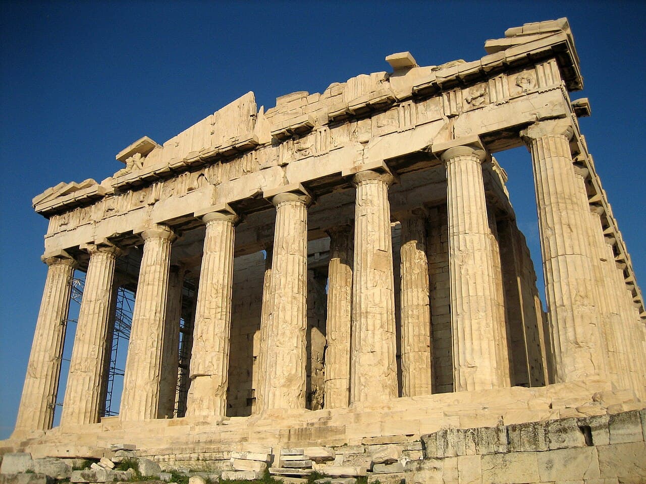 The west front of the Parthenon in warm sunlight against a deep blue sky, with its row of fluted columns and broken pediment.